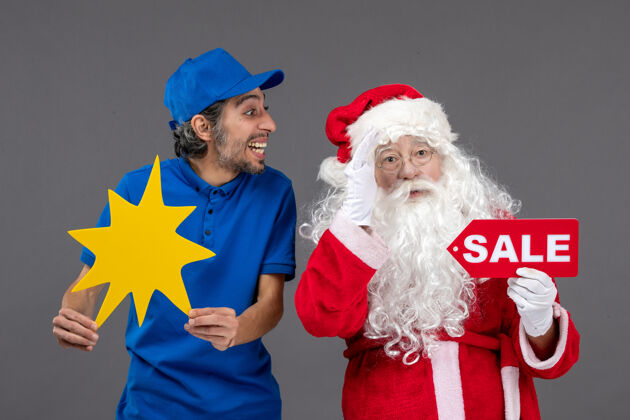 十二月圣诞老人的正面图 男性信使手持销售横幅 灰色墙上有黄色标志人快乐帽子