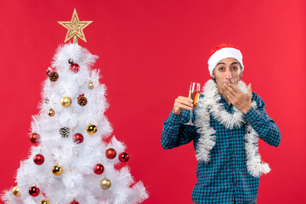 放圣诞节心情与情绪激动的年轻人圣诞老人帽子在一个蓝色的衬衫剥离举行一杯葡萄酒放手指抱圣诞圣诞老人