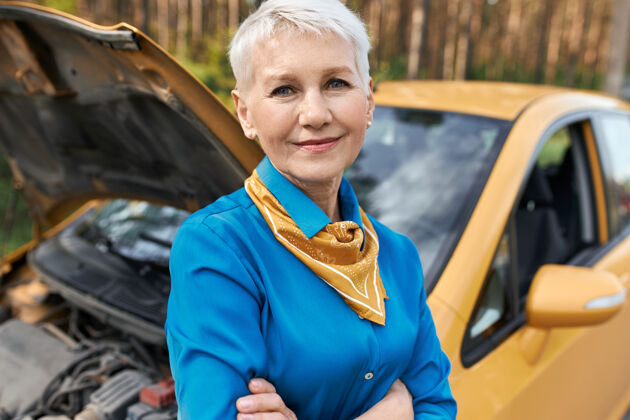 损坏沮丧不快乐的女性退休者站在她的车旁 打开引擎盖 双臂交叉 等待路边救援无助成人援助