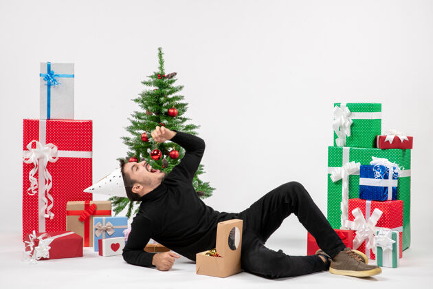 新郎正面图：年轻人围坐在节日礼物旁 试图在白墙上吃玩具礼物模型十二月