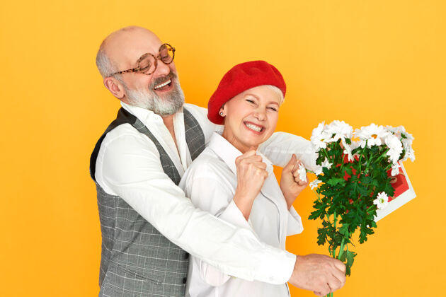 男朋友一幅英俊 有魅力 秃顶 留着灰胡子的老人拥抱着戴着红色贝雷帽的美丽妻子的画像浪漫花束约会