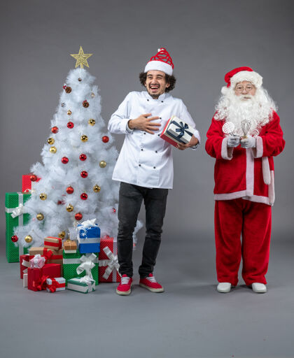 快乐圣诞老人与男性厨师和圣诞礼物在灰色墙上的正面视图正面礼物圣诞老人