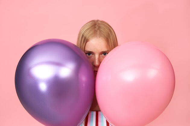 庆典神秘的年轻金发女性 脸上有雀斑 脸上有刺眼的粉红色 躲在两个闪亮的金属氦气球后面 这是一幅孤立的肖像聚会女人可爱