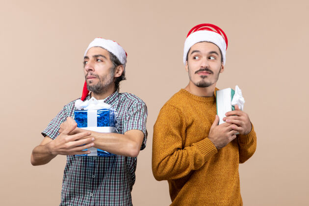 脸正面图两个被冒犯的家伙把他们的圣诞礼物藏在米色的隔离背景上微笑两个视图