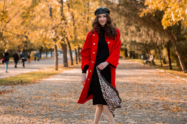 休闲迷人时尚微笑的女人卷发漫步在公园穿着暖红色外套秋季时尚 街头风格 戴贝雷帽和豹纹围巾女人时尚苗条