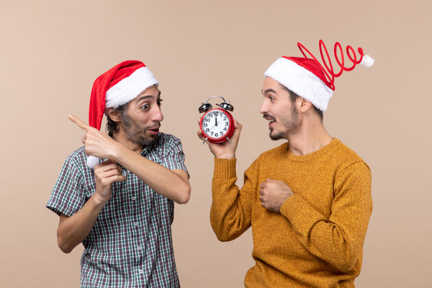 男人正面图两个快乐的男人 一个拿着闹钟 另一个拿着闹钟 背景是米色的男性夫妇视图