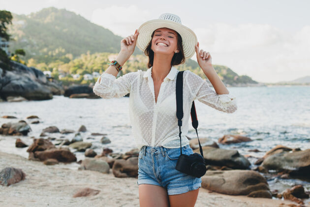 夏天在亚洲度暑假的年轻漂亮的时髦女人 在热带海滩上放松 数码相机 随意的波西米亚风格 海洋风景 苗条的棕褐色身体 独自旅行帽子时尚模特
