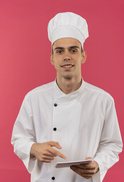 男面带微笑的年轻男厨师穿着厨师制服拿着并指着笔记本制服笔记本分