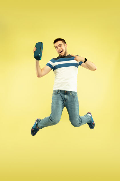 电脑天空之声黄色背景的快乐跳跃人的全长肖像现代科技 自由选择的概念 情感的概念使用便携式扬声器像飞行中的超级英雄快乐男孩手
