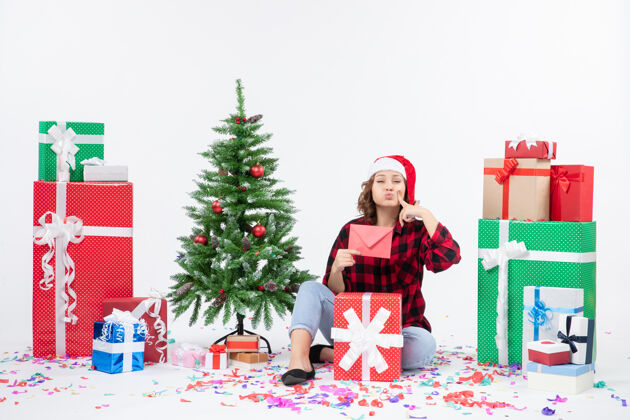 微笑前视图年轻女子坐在周围的礼物举行信封上的白墙节日冬天圣诞节