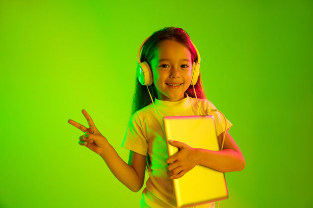 Kid美丽的女性半身像 隔离在霓虹灯下的绿色背景上年轻动情的少女人类的情感 面部表情概念时尚的色彩手持平板电脑和微笑表情女性海洋