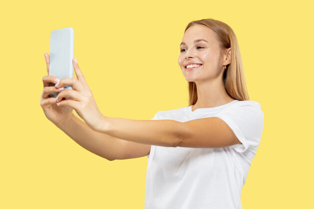 工作黄色工作室背景上的白人年轻女子半身肖像穿着白衬衫的漂亮女模特人类情感的概念 面部表情微笑 自拍或视频博客内容女商人金发公司