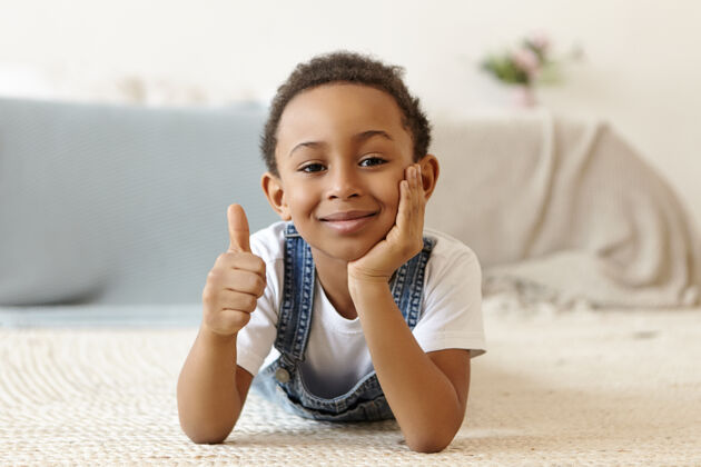 随意八岁的美国黑人男孩躺在家里的地板上 看上去非常友好赢家年龄拇指