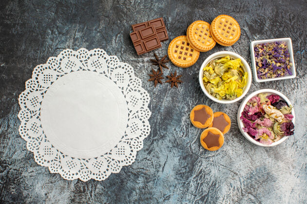 美味在灰色背景上有白色蕾丝的干花 巧克力和饼干碗的俯视图灰色桌子巧克力