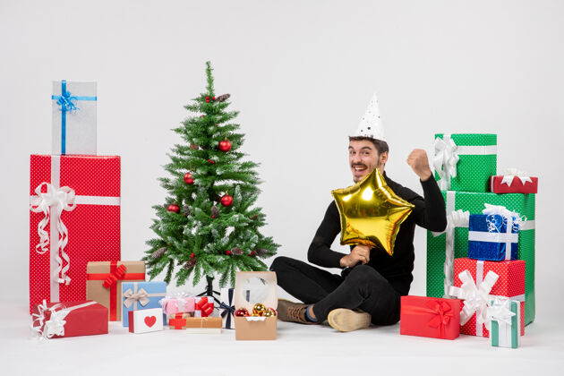 圣诞快乐年轻人围坐在礼物旁边 拿着金星在白墙上快乐坐人