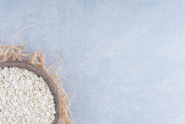 燕麦燕麦片堆在一个小木碗里 放在大理石背景的稻草堆上配料碗燕麦