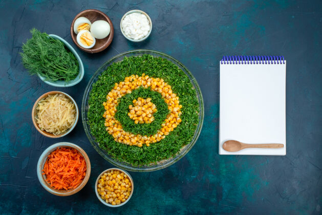 食物在深蓝色的桌子上放着一个圆形玻璃盘子 里面放着鸡蛋和胡萝卜片 里面放着玉米的顶视图蔬菜沙拉蔬菜深色绿色