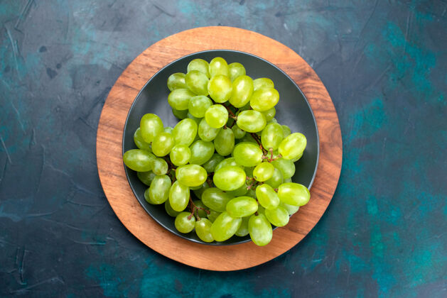 地上顶视图新鲜的绿色葡萄醇厚多汁的水果在深蓝色桌板内盘子绿色顶部