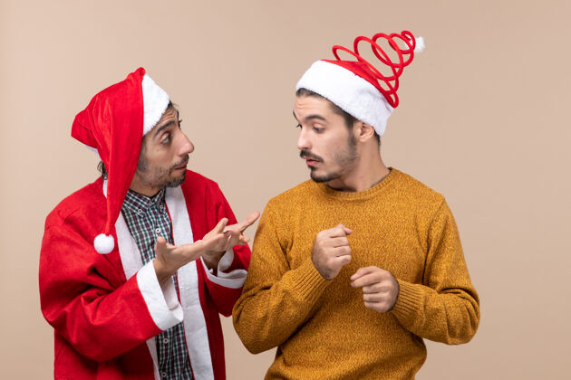 米色两个戴着圣诞帽的朋友在米色孤立的背景下交谈男性视图脸