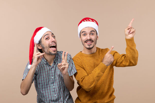 前面正面图：两个戴着圣诞帽的快乐男人在与世隔绝的背景下展示了一些非常有趣的东西帽子男人微笑