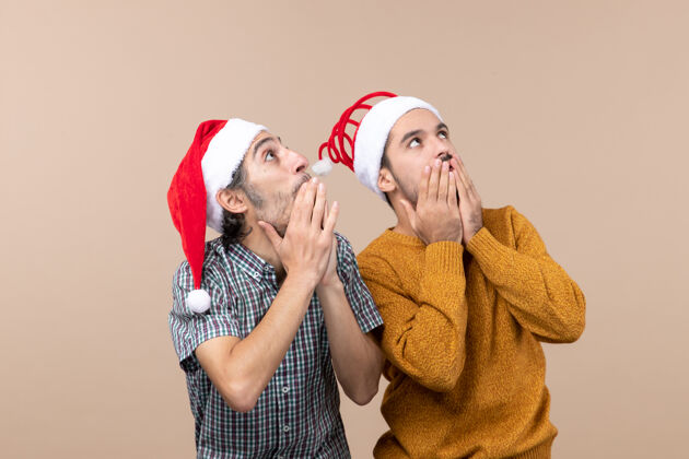 微笑正面图：两个戴着圣诞帽的好奇的男人在孤立的背景下饶有兴趣地看着什么东西兴趣成人男人