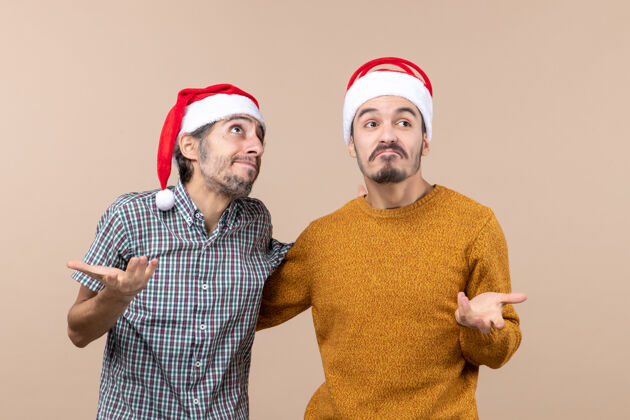 两个正面图：两个情绪化的粗心的家伙戴着圣诞帽 背景是米色的男人圣诞老人米色