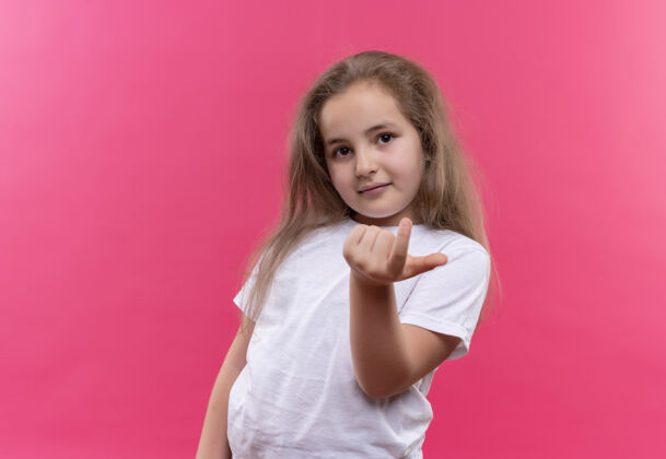 看一个穿着白色t恤的小女孩 在孤立的粉色背景上展示了过来的姿态学校白色手势