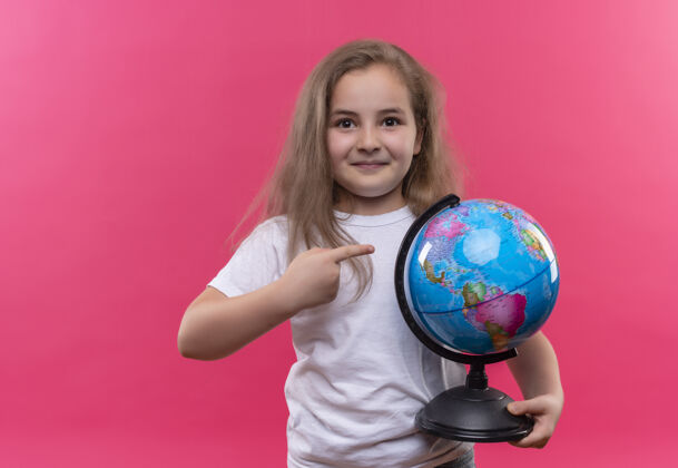 女孩微笑着的小女孩穿着白色t恤拿着地球仪 背景是孤立的粉色白色地球仪粉色