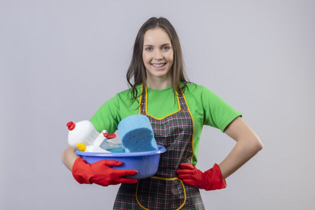 臀部微笑的清洁年轻女孩穿着制服 戴着红色手套 拿着清洁工具 把她的手放在屁股上 在孤立的白色背景上微笑手套女孩