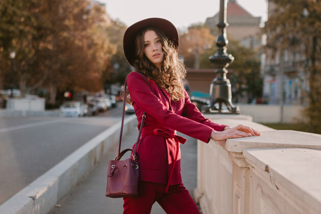 穿着穿着紫色西装的漂亮时髦女人走在城市街头 春夏秋冬时节时尚潮流戴着帽子 手拿钱包服装深色秋天