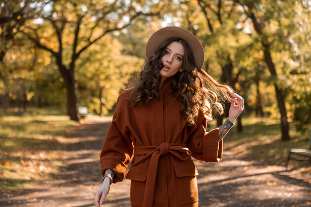优雅迷人时尚微笑的瘦身女子卷发漫步公园身着暖棕色外套 秋日时尚街头风衣服年轻阳光