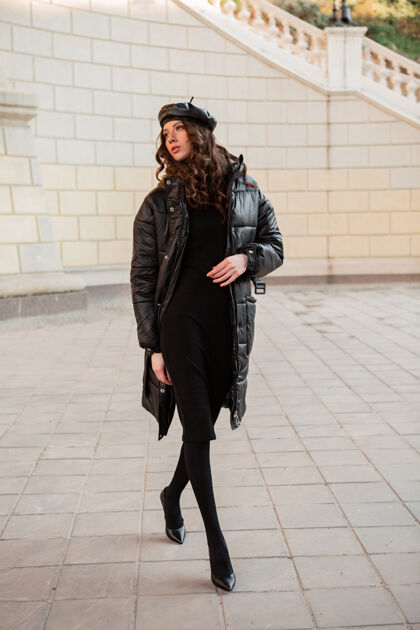 服装时尚女人摆出冬秋时尚潮流黑色羽绒服和皮帽贝雷帽在古老美丽的街道穿着高跟鞋优雅夹克女性