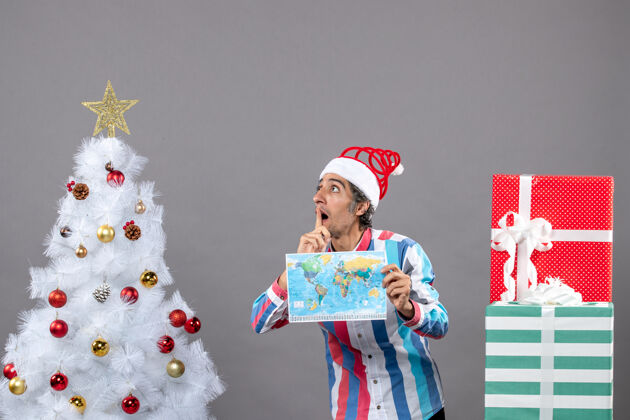 人前视图困惑的男子与螺旋弹簧圣诞帽举行世界地图旅行者快乐灰色