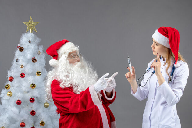 圣诞圣诞老人和女医生在灰色墙上打针的前视图注射健康快乐