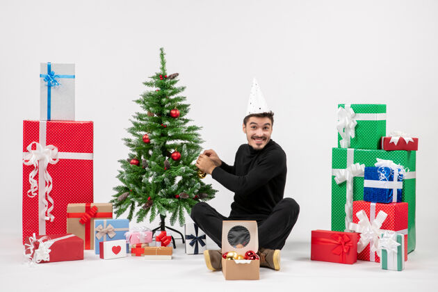 快乐年轻人围坐在节日礼物装饰在白色墙上的小树的前视图圣诞小节日