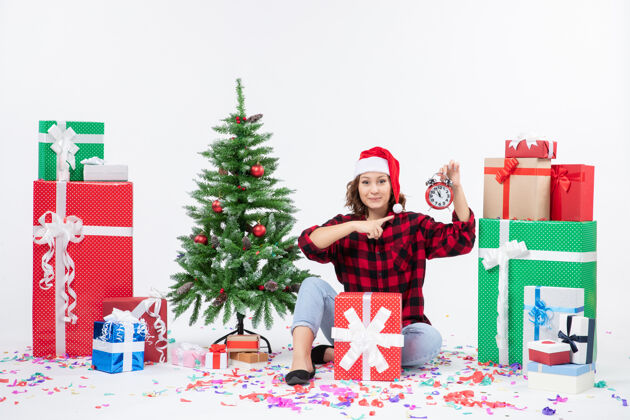 快乐前视图的年轻女子坐在圣诞礼物周围拿着白色墙上的时钟礼物圣诞礼物