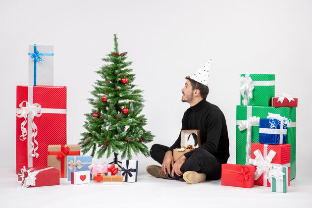 冬天年轻人坐在白色墙上的节日礼物周围的正面视图十二月雪模型