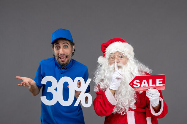 人圣诞老人与男性信使持有和销售横幅在灰色墙上的正面视图圣诞老人节日销售