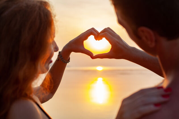 约会年轻性感浪漫的情侣在夏天的沙滩上快乐地在一起 穿着泳衣在日落时露出心形标志浪漫户外年轻