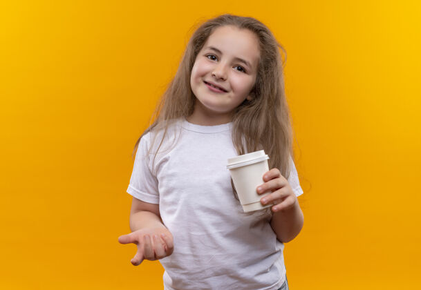 白色微笑的小女生穿着白色t恤 在孤立的橙色背景上捧着一杯咖啡拿着微笑杯子