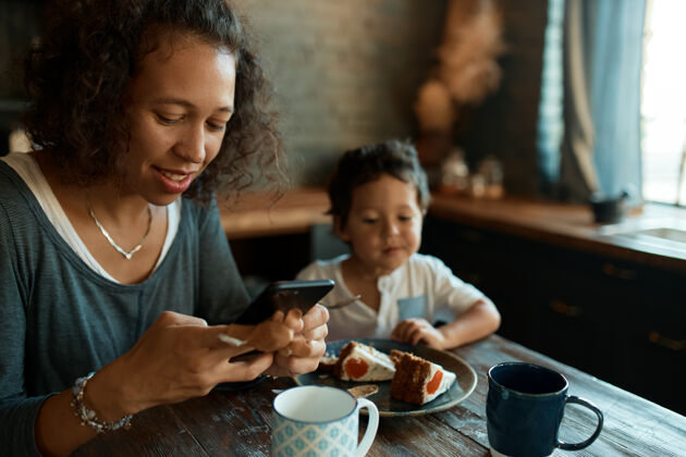 母亲忙碌的年轻单身母亲用手机进行异地工作 在社交网络账号上发帖忙碌智能手机沟通