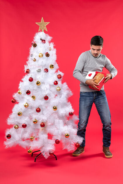 灰色穿着灰色上衣的年轻帅哥站在装饰过的白色圣诞树旁 打开礼物装饰线条帅气成人