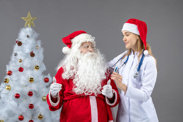 十二月圣诞老人和女医生的前视图 女医生拿着测温仪在灰色的墙上圣诞快乐护士人