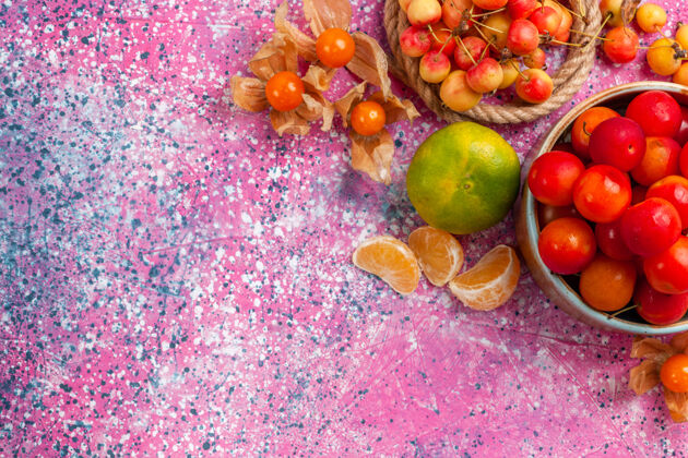 盘子顶视图新鲜的酸李子圆润的水果放在小盘子里 粉红色的桌子上放着樱桃和橘子小水果水果