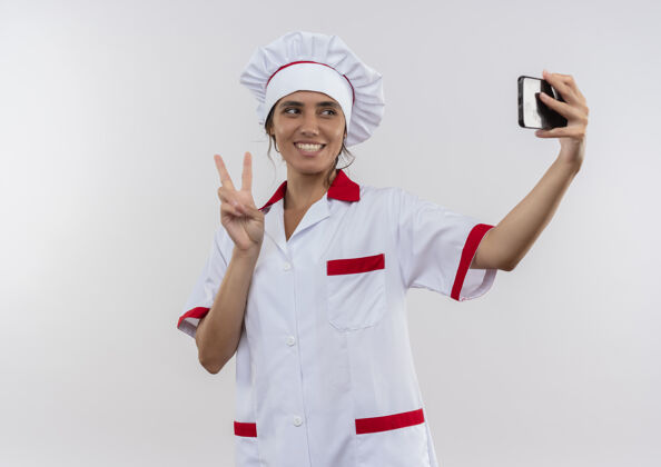 女微笑的年轻女厨师穿着厨师制服 自拍展示和平姿态与复制空间穿着和平手势