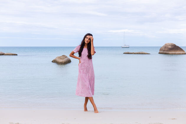 快乐一个年轻浪漫的女人 留着长长的黑发 穿着裙子 在沙滩上微笑着 笑着 一个人度过了一段美好的时光海滩假期时尚