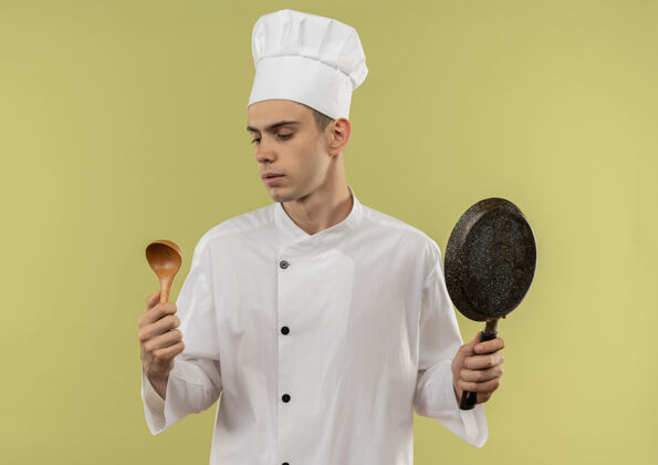 厨师想着年轻的男厨师穿着厨师制服拿着煎锅看着手中的勺子穿厨师思考