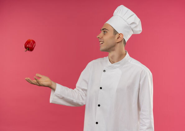 简介站在侧视图微笑的年轻男厨师穿着厨师制服扔了一个西红柿男厨师番茄