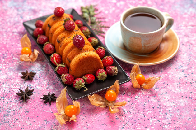 蛋糕正面图：美味的蛋糕放在黑蛋糕锅里 新鲜的红色草莓和一杯茶放在粉红色的桌子上茶新鲜烘焙