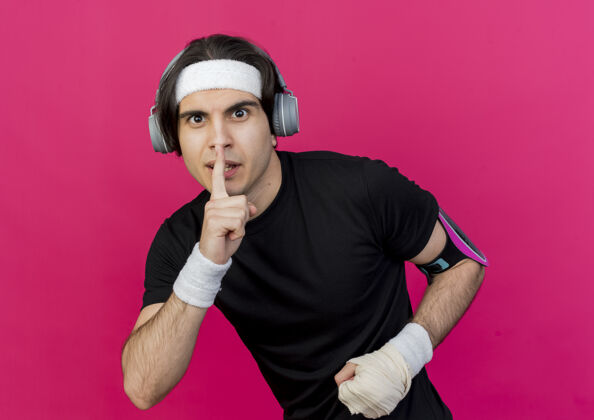 手势年轻的运动型男子 戴着运动服和头带 戴着手机和智能手机袖标 手指放在嘴唇上做着沉默的手势智能手机头带运动